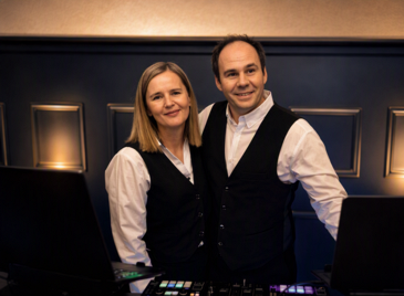 Eva und Christian stehen hinter dem DJ-Pult auf ihrer Hochzeit mit DJ Niederbayern in festlicher Atmosphäre